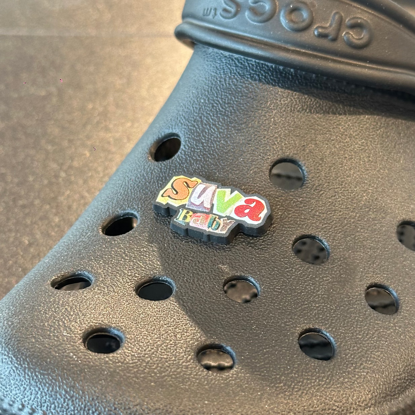 Black croc shoe with a colorful 'Save' pin on a gray surface
