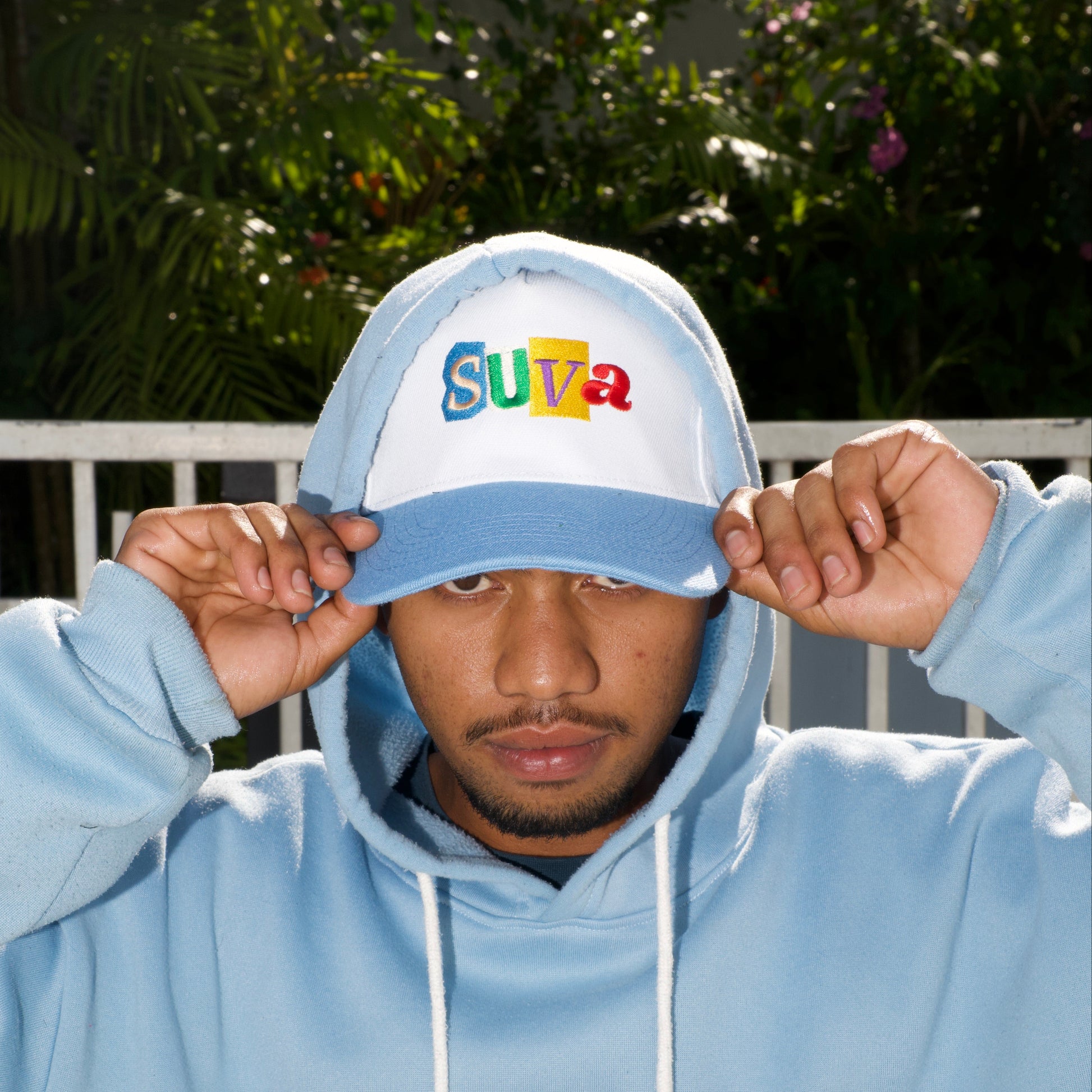 Person wearing a light blue hoodie with text, holding a cap outdoors.