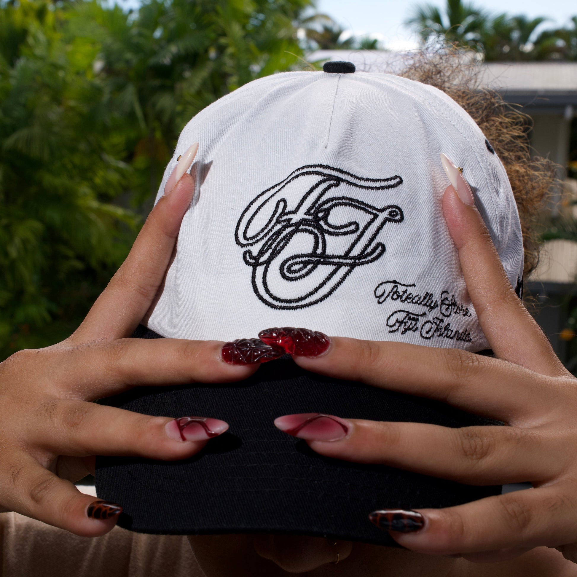 White cap with black logo held by a person outdoors