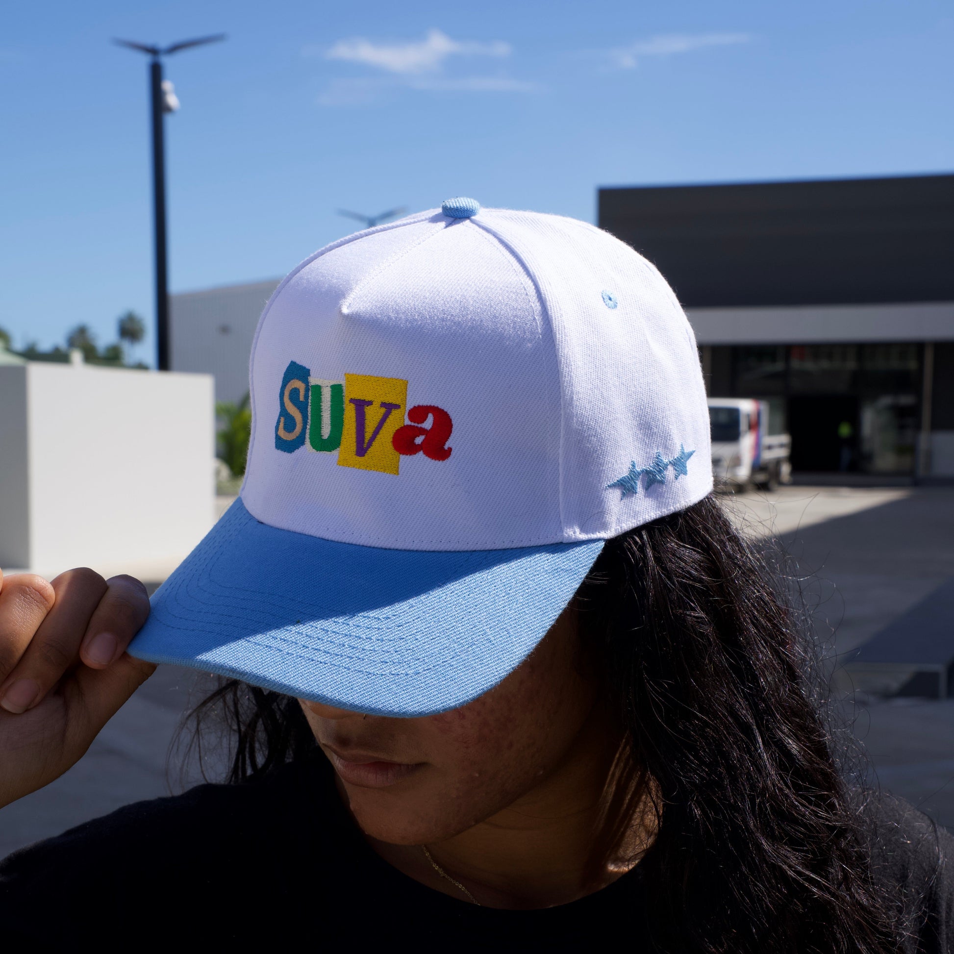 Person wearing a cap with colorful text, standing outdoors.