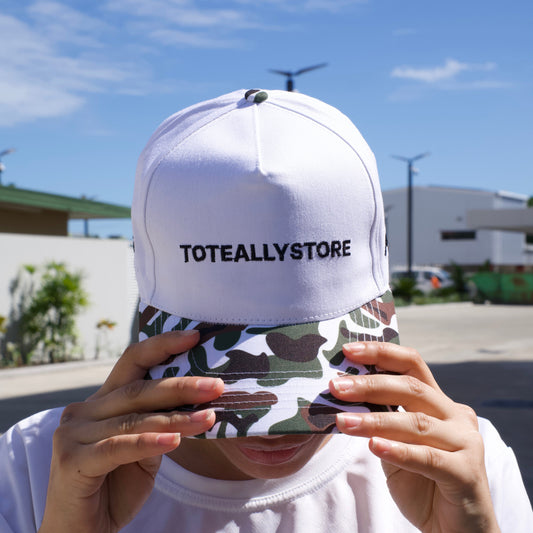 Person holding a camouflage phone case with a white cap labeled 'TOTALLY STORE' against a blue sky.
