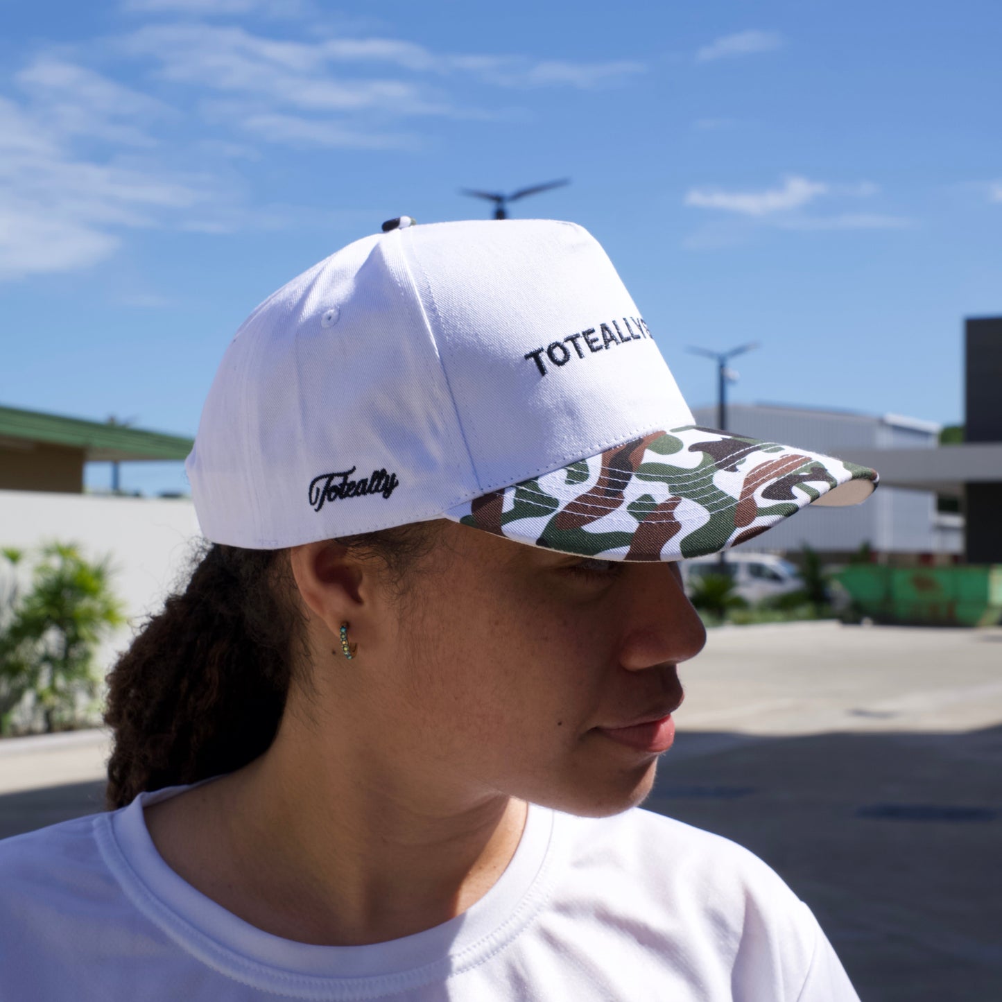 Person wearing a white cap and shirt with a logo, looking at a clear blue sky.