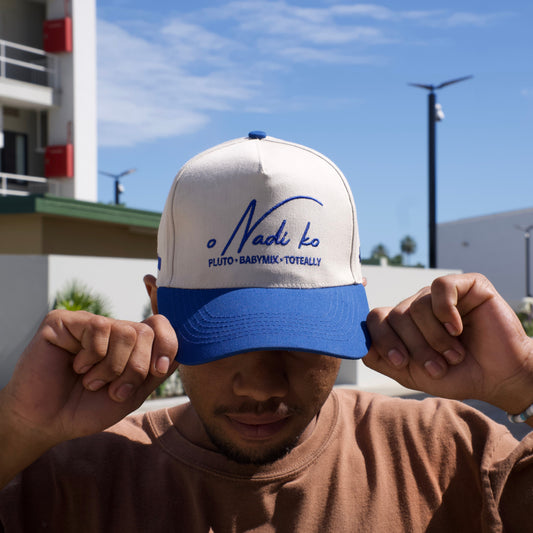 Person holding a white cap with blue visor and text against a clear blue sky.