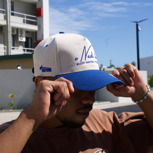Person holding a blue and white cap with a logo against a clear blue sky.