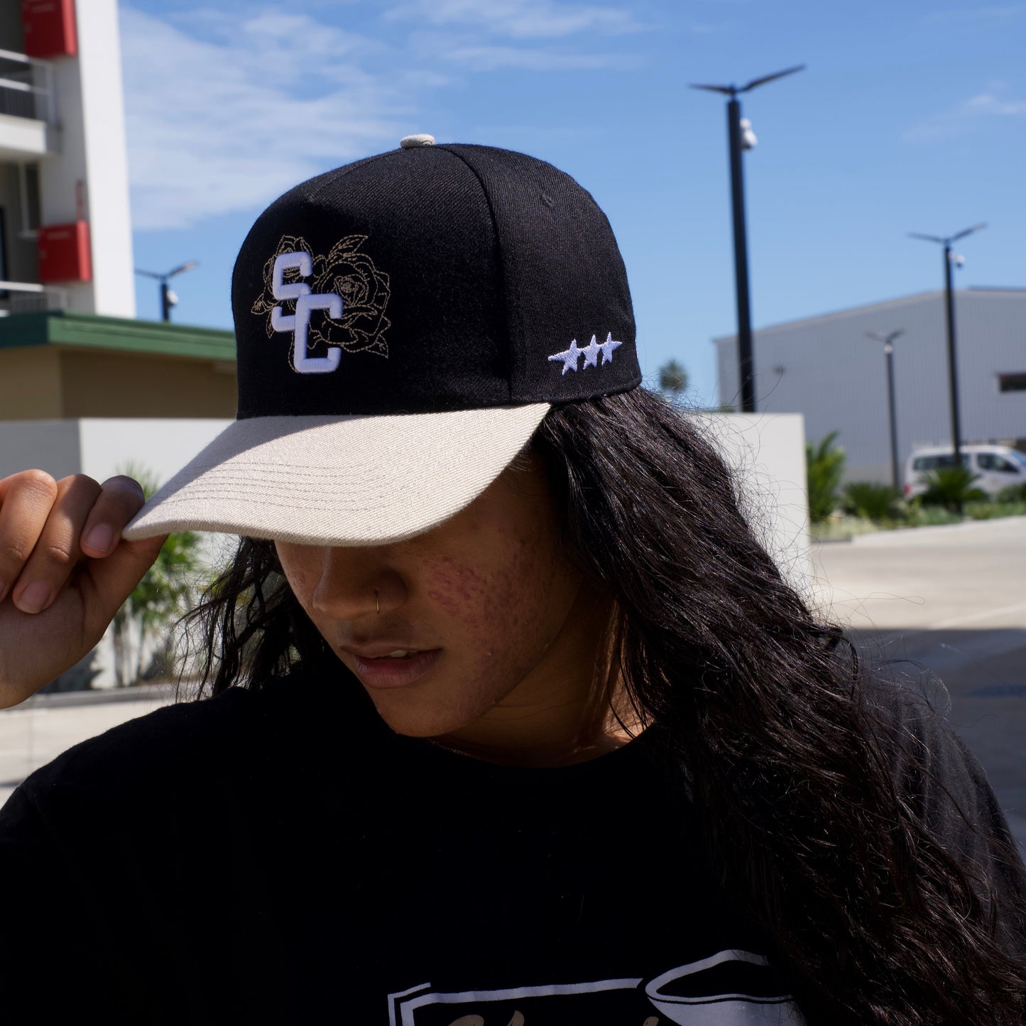 Person wearing a black cap with a logo and text, outdoors with a clear sky.