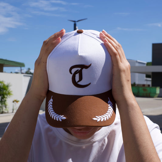 Person holding a white cap with a logo against a blue sky