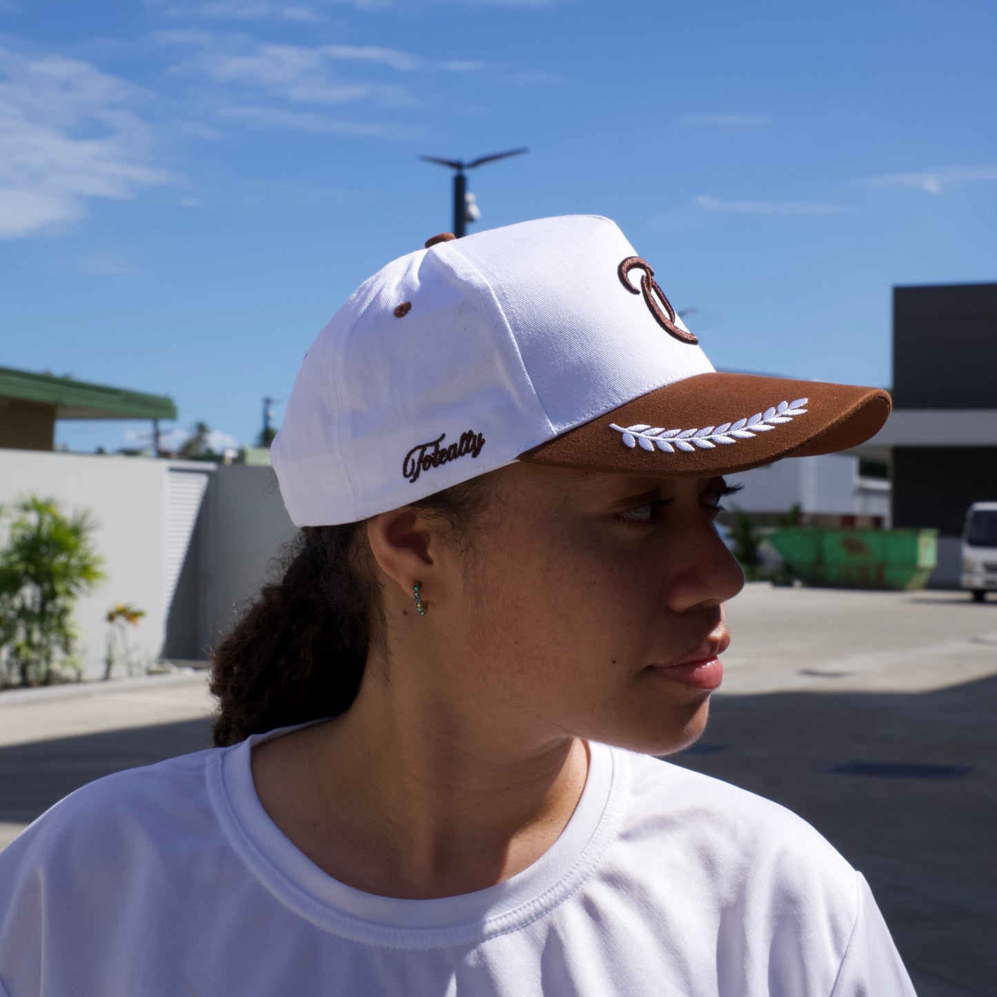 Person wearing a white cap with a logo against a blue sky