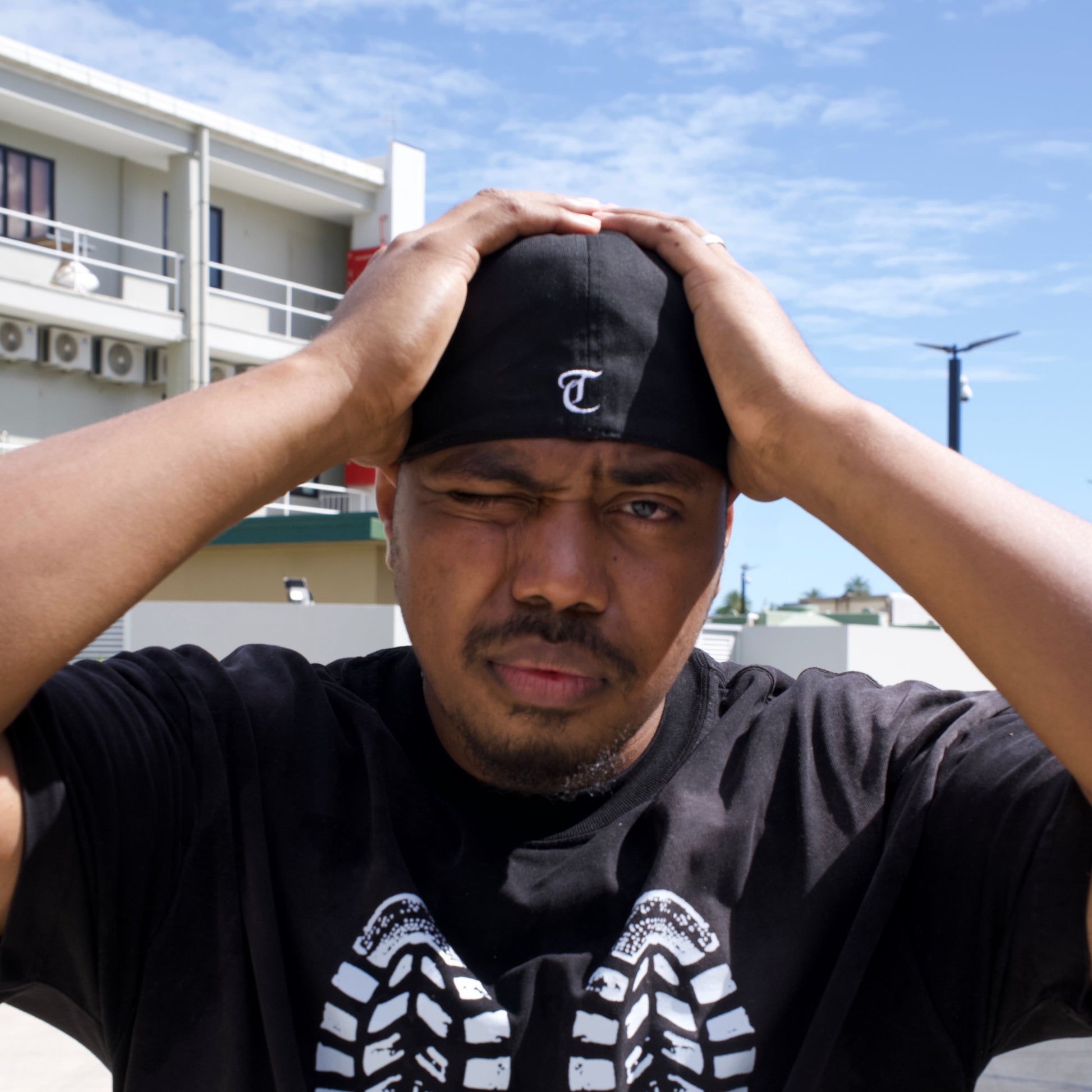 Person holding a black shoe with a brand logo against a blue sky.