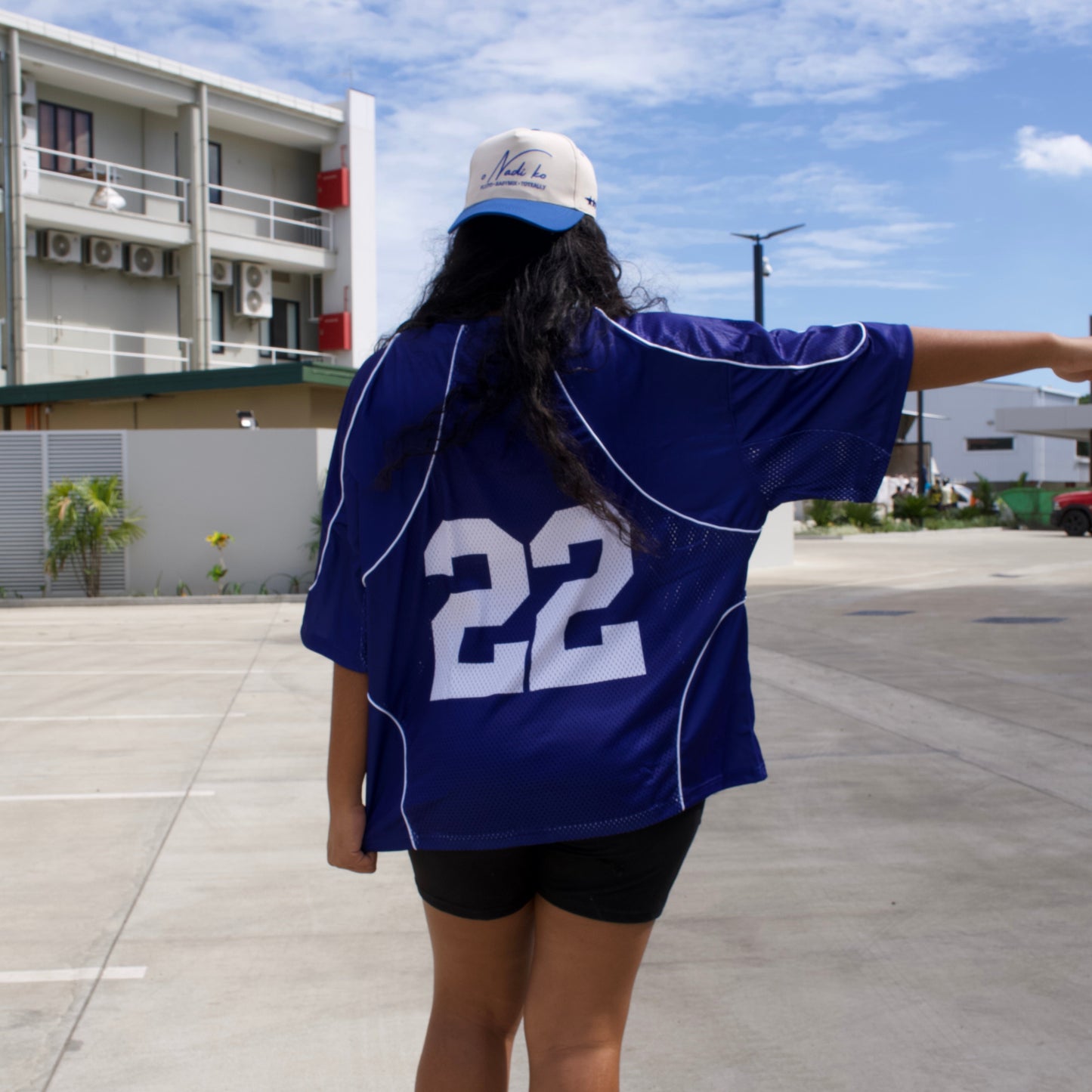 Person wearing a blue sports jersey with number 22 on a sidewalk with buildings and trees in the background.