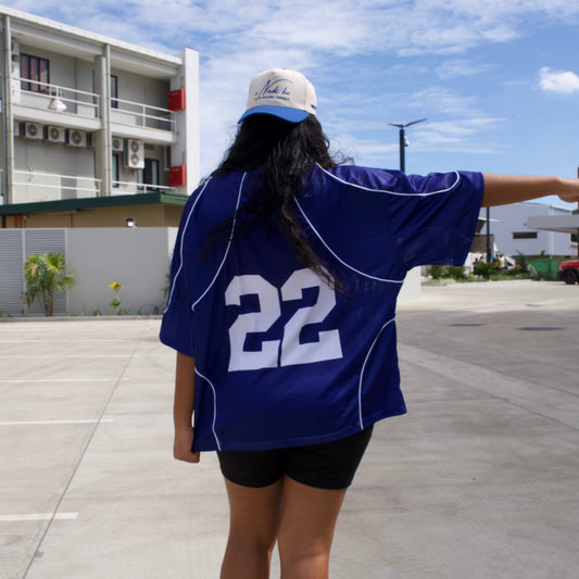 Person wearing a blue sports jersey with number 22 on a sidewalk with buildings and trees in the background.