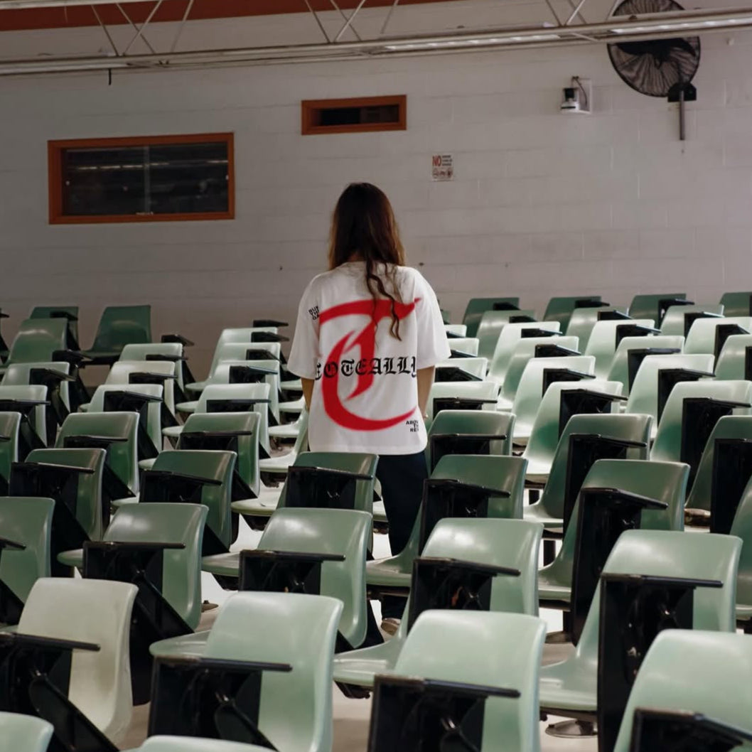 Person standing in an empty classroom with green chairs and a whiteboard on the wall.