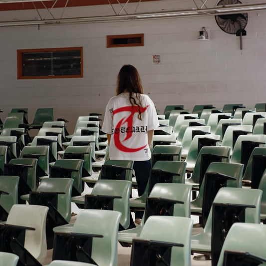 Person standing in an empty classroom with green chairs and a whiteboard on the wall.