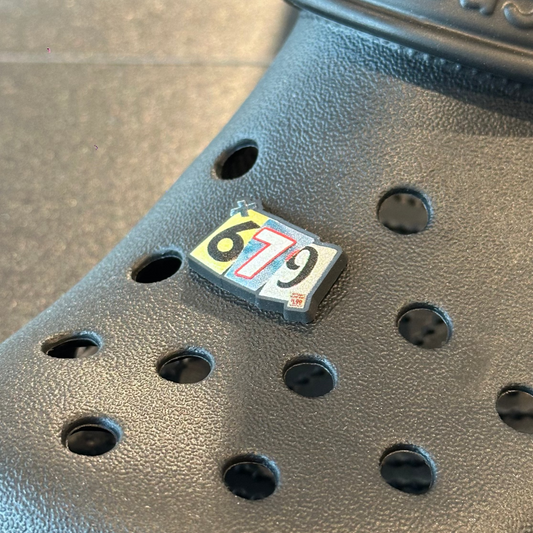 Black Crocs shoe with a size tag on a tiled floor