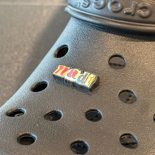 Black Crocs shoe with a colorful label on a reflective surface