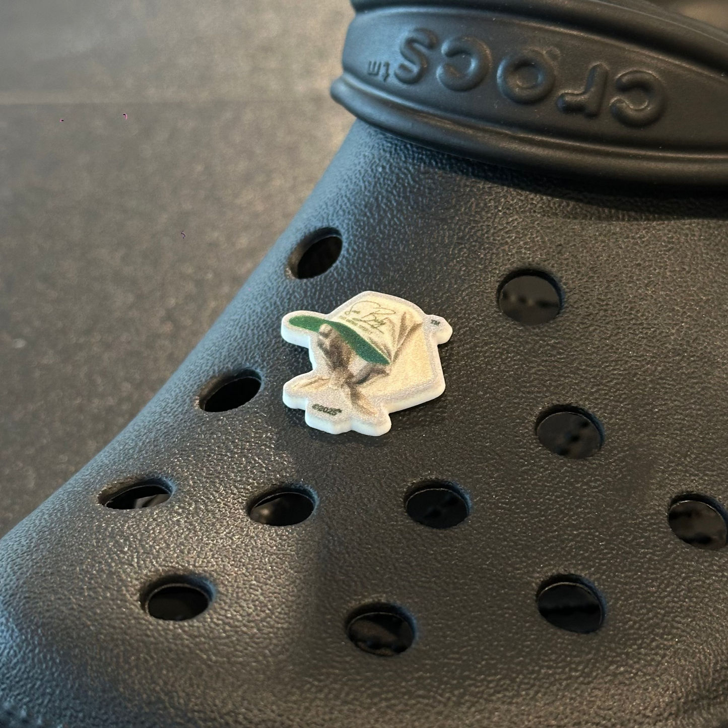 Black Crocs shoe with a small decorative item on a gray surface