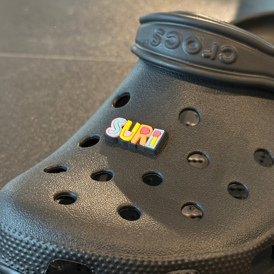 Black Crocs sandal with a colorful 'Surf' pin on a dark surface